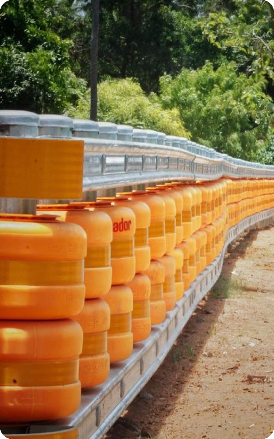 Ador-branded orange safety roller barrier installed along a curved road section