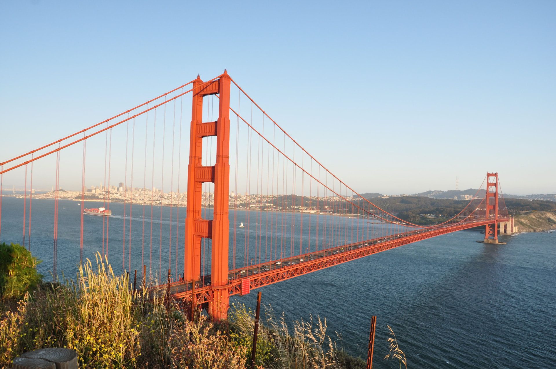 Long-span suspension bridge carrying traffic across a bay at golden hour.